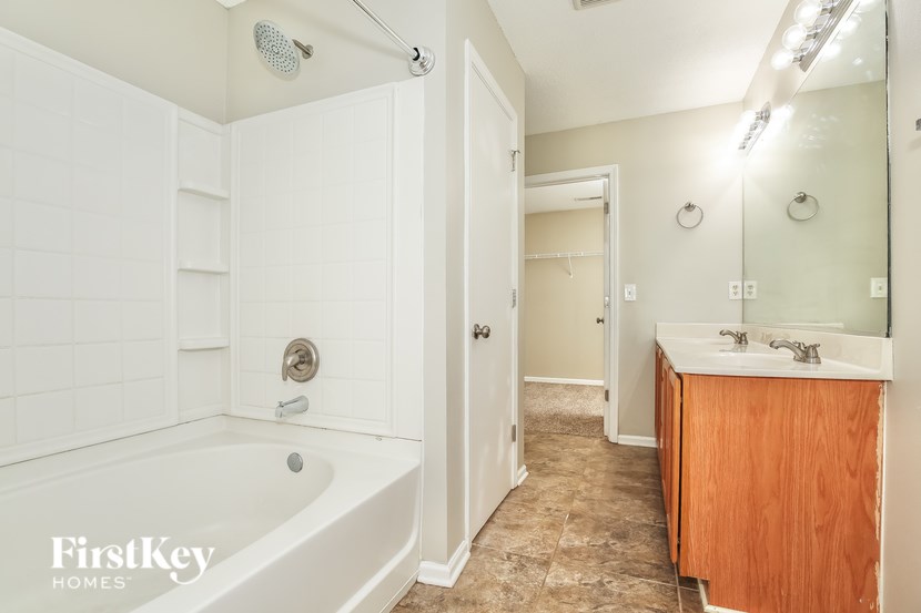 A white bathroom with a wooden vanity and a white bathtub.