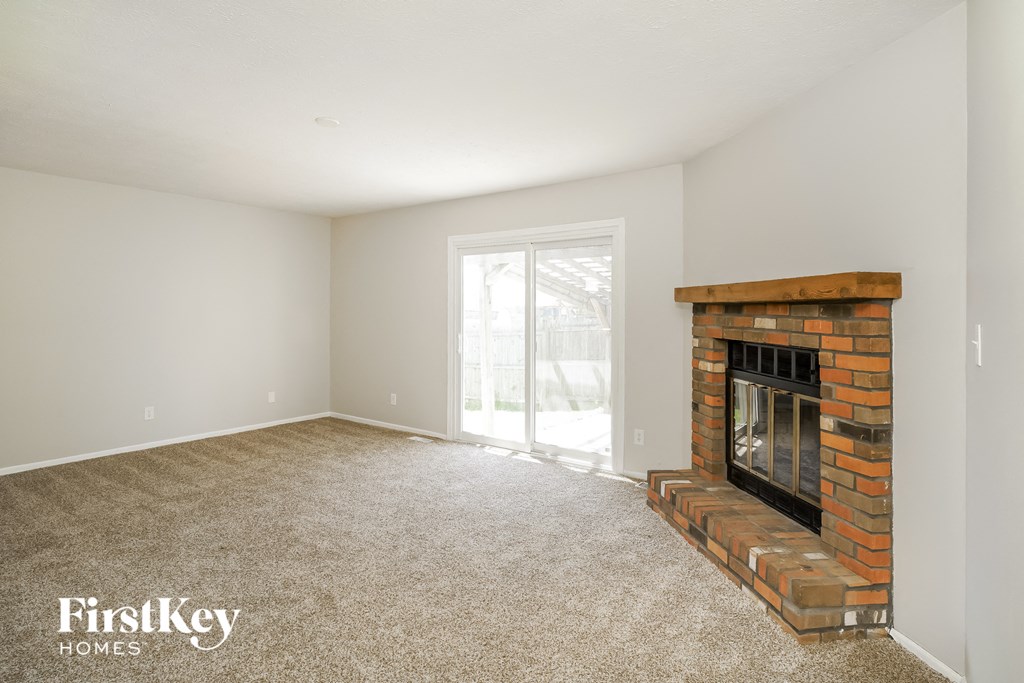 an empty living room with a brick fireplace and a window