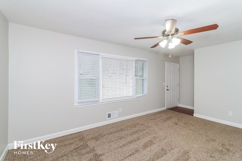A room with a carpet floor, a ceiling fan, and a window with blinds.