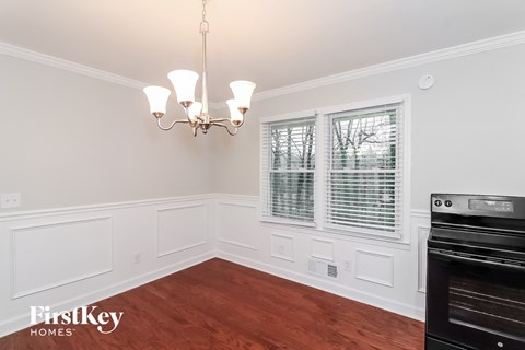 A chandelier hangs over a white-walled room with wood flooring.