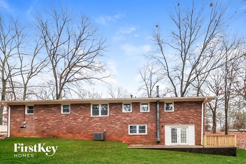 A brick house with a white door and windows is surrounded by trees.
