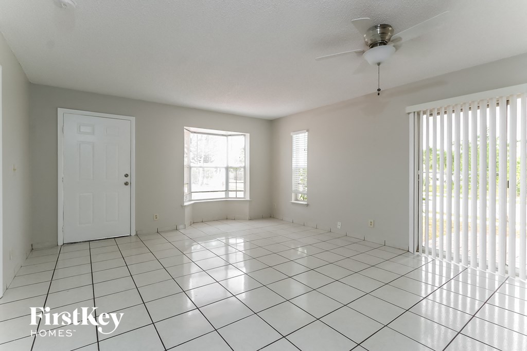 an empty living room with a white tile floor and a ceiling fan