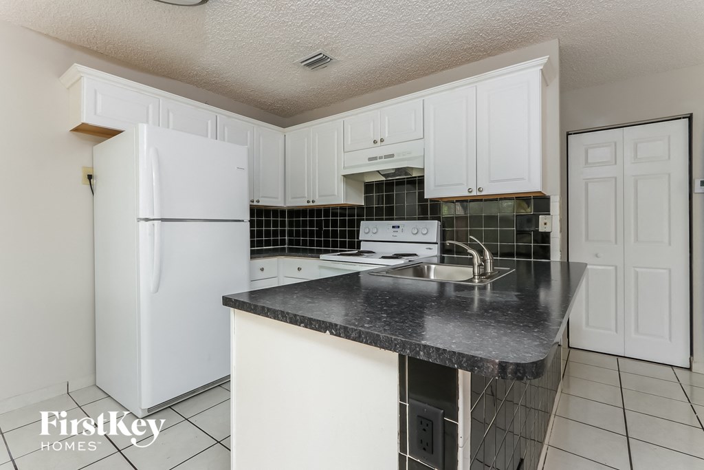 a kitchen with white cabinets and black countertops and a white refrigerator