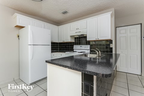 a kitchen with white cabinets and black countertops and a white refrigerator