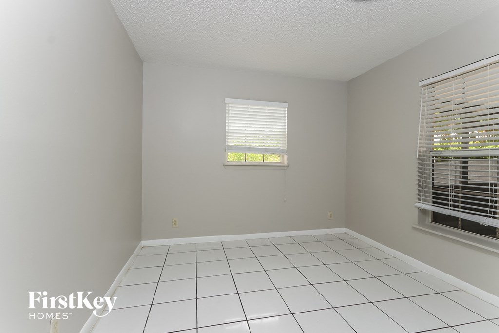 an empty room with a white tiled floor and two windows