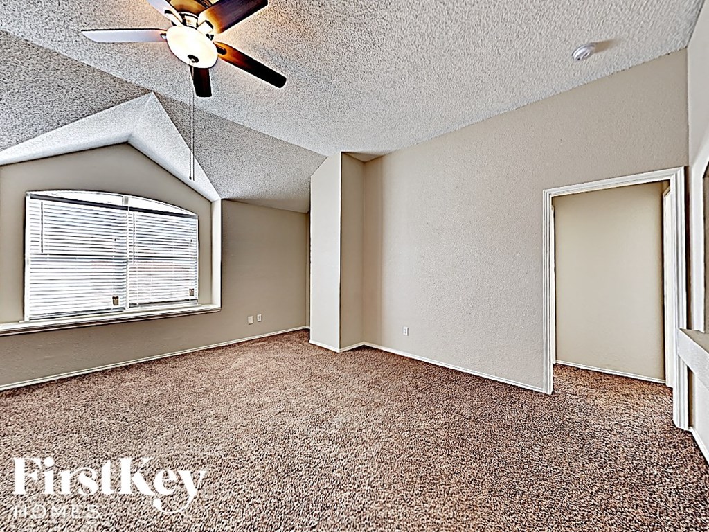 an empty living room with a large window and a ceiling fan