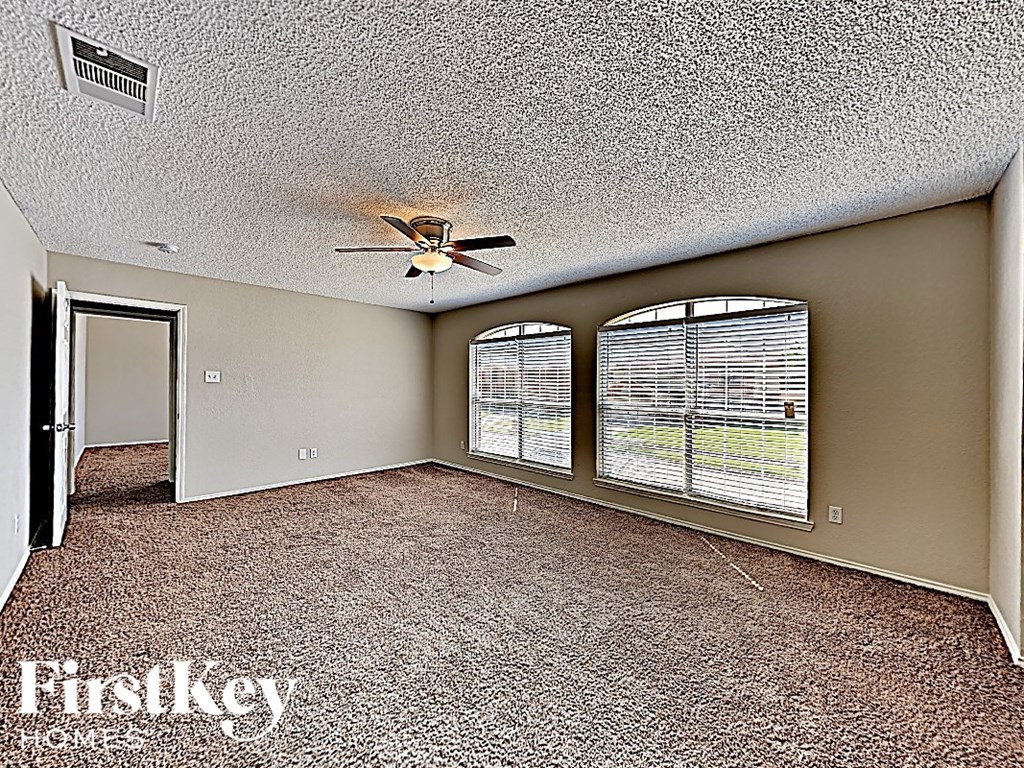 an empty living room with a ceiling fan and windows