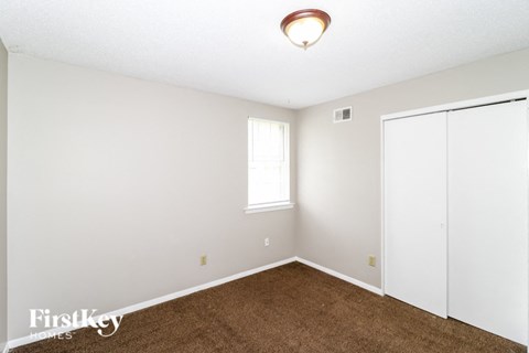 a bedroom with white walls and carpet and a window and a closet