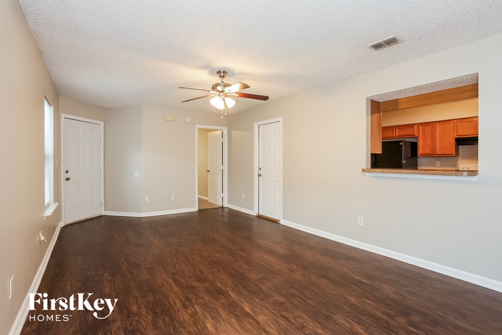 an empty living room with a ceiling fan and a kitchen