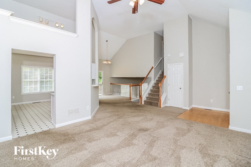 A spacious living room with a staircase and a ceiling fan.