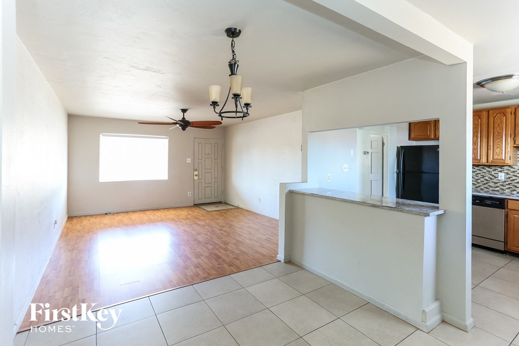 an empty living room with a kitchen and a ceiling fan