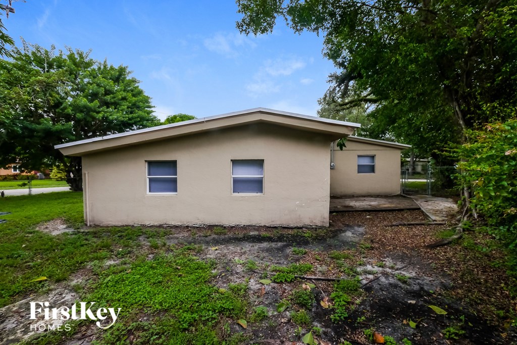 A small house with a beige exterior is surrounded by greenery.