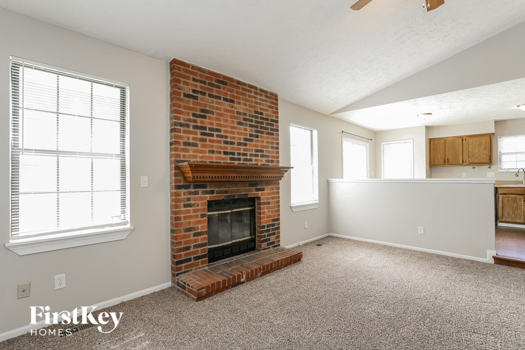an empty living room with a brick fireplace and a kitchen