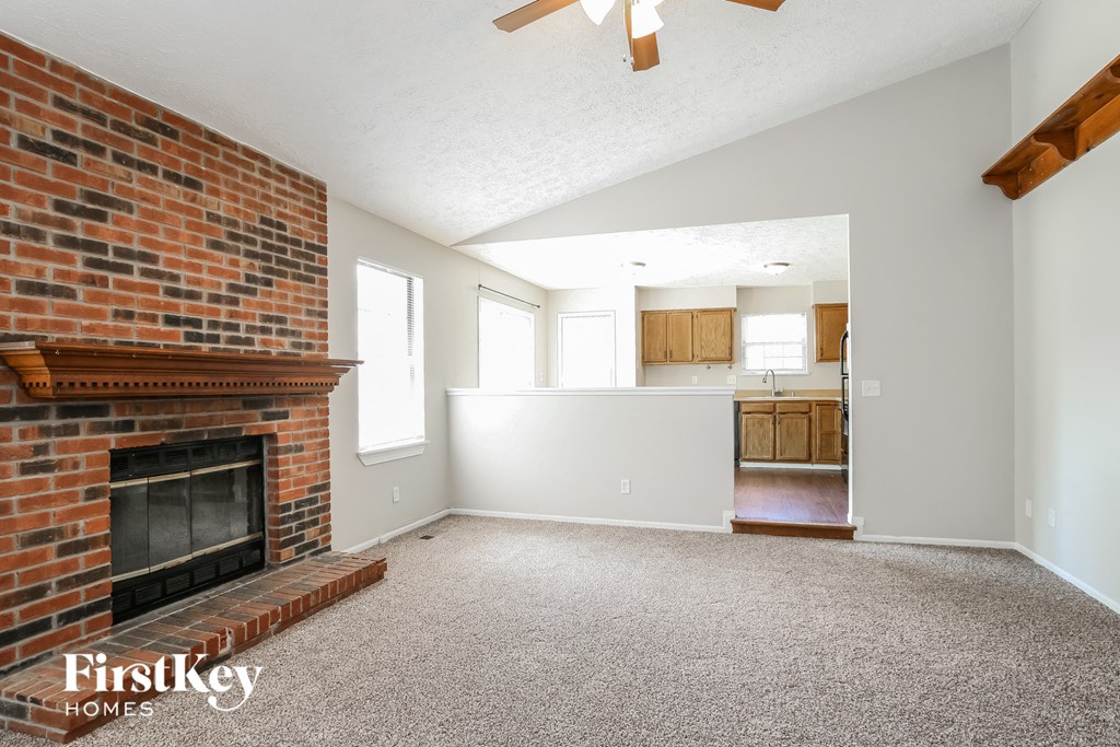 an empty living room with a brick fireplace and a kitchen