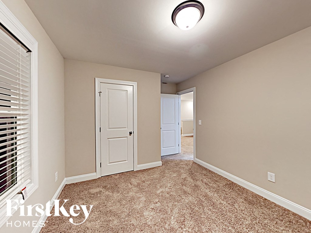 A carpeted room with a door and a window with blinds.