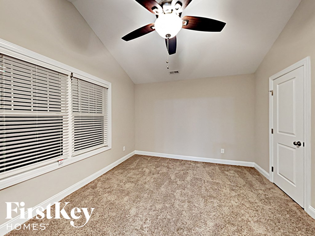 A room with a carpeted floor, a ceiling fan, and a door.