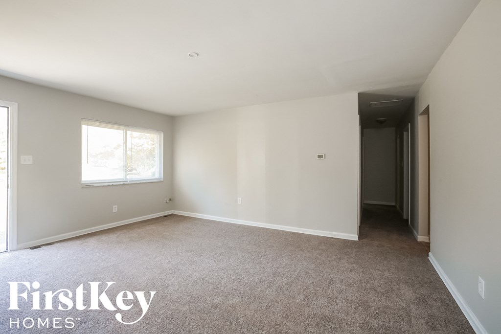 an empty living room with carpet and a door to a hallway