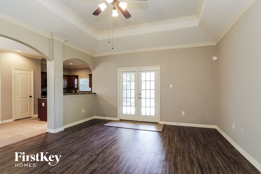 an empty living room with a ceiling fan and a door to a kitchen