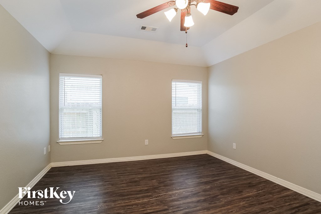 the spacious living room with hardwood flooring and a ceiling fan