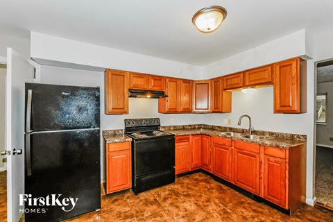 A kitchen with orange cabinets and a black fridge.