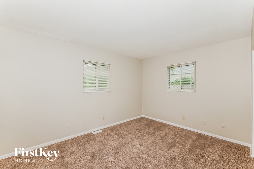 A room with a carpeted floor and two windows.