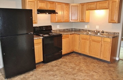 A black refrigerator is in a kitchen with wooden cabinets.