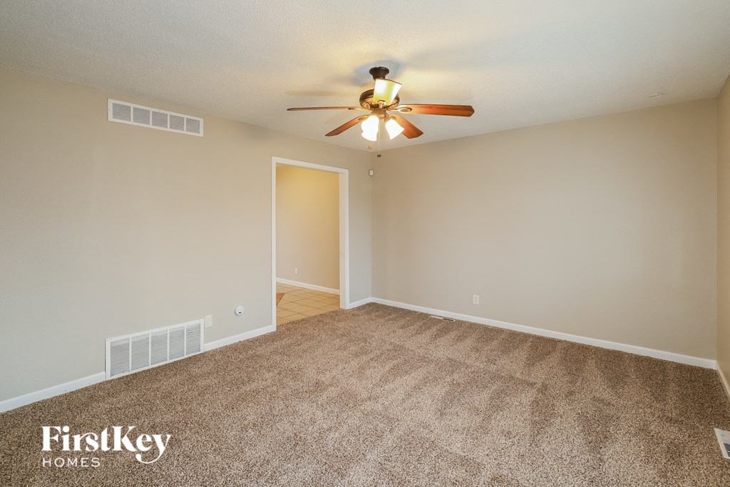 A carpeted room with a ceiling fan and a door.