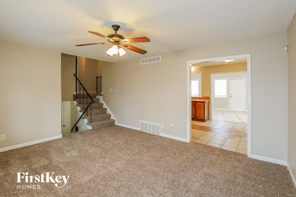 A spacious room with a carpeted floor, a ceiling fan, and a staircase leading to another room.