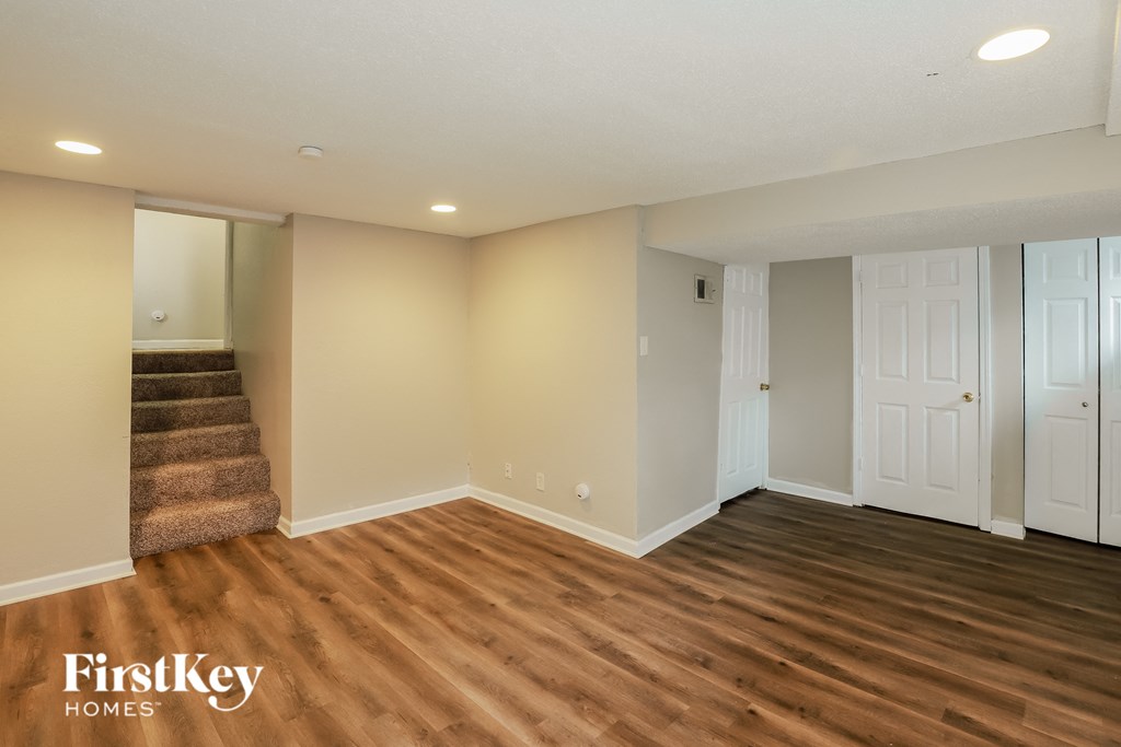 A spacious room with wooden flooring and white walls, featuring a staircase and two doors.