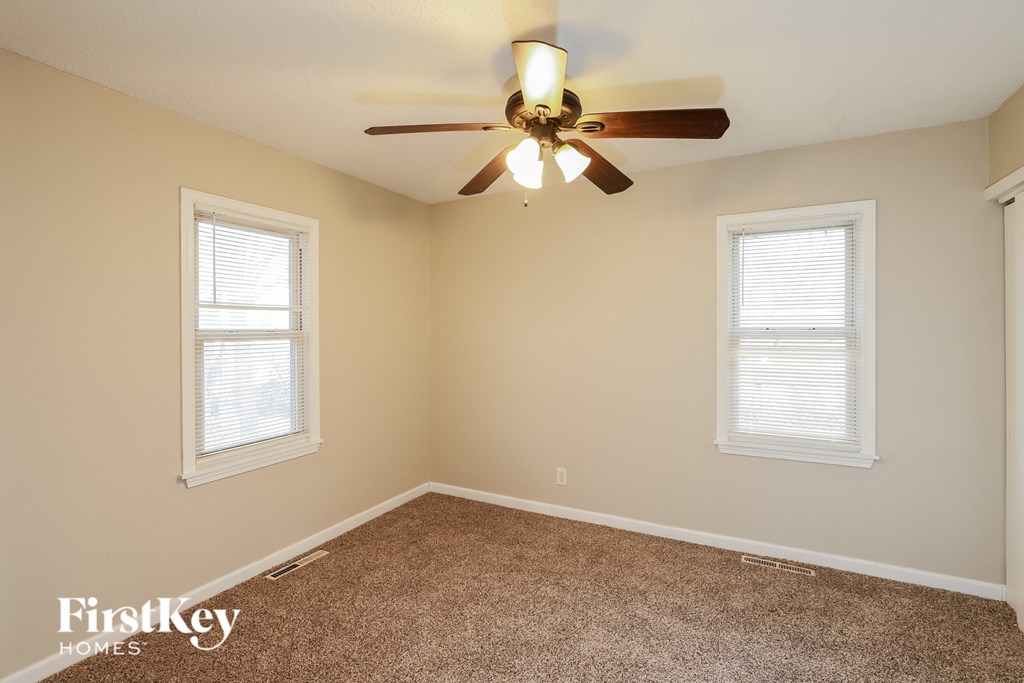 A room with a ceiling fan and two windows.