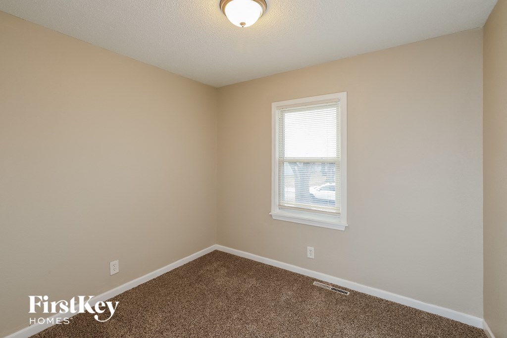 A room with a carpeted floor, a window with blinds, and a light fixture on the ceiling.