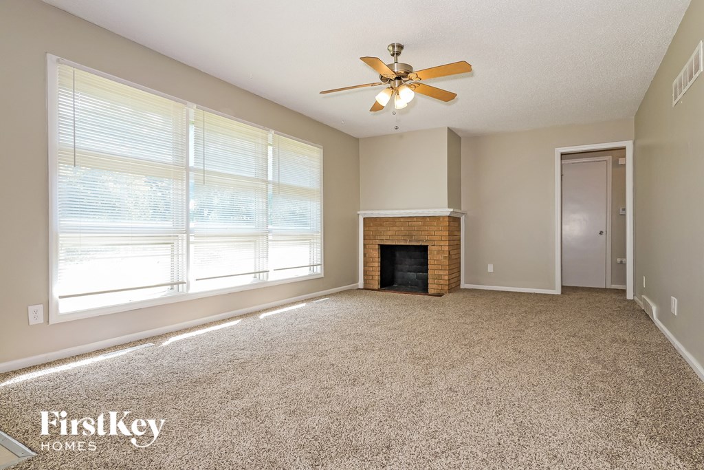 A spacious living room with a fireplace and a ceiling fan.