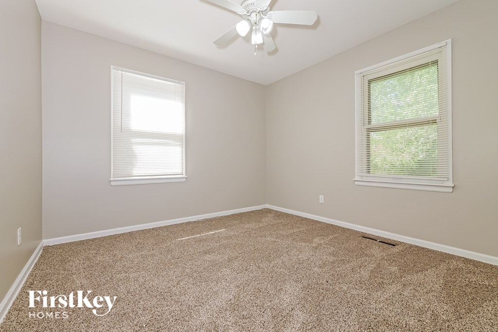 A room with a carpeted floor, a ceiling fan, and two windows.