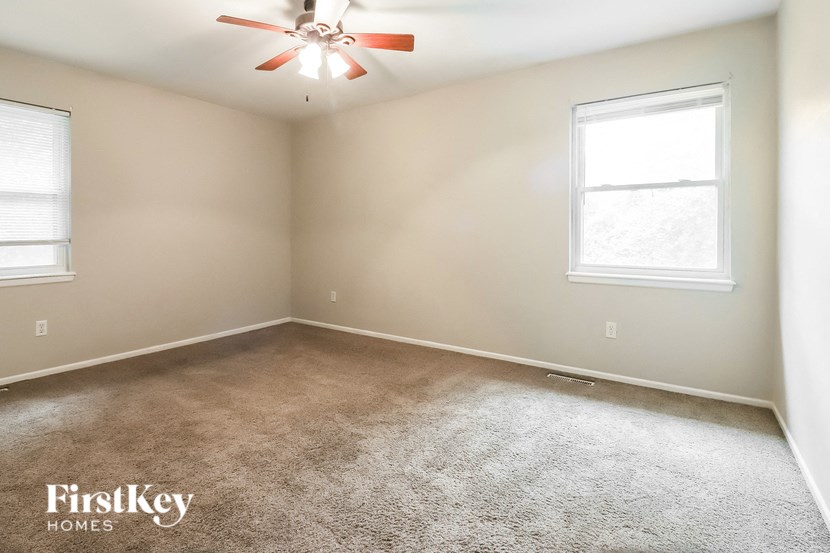 a carpeted room with a ceiling fan and two windows