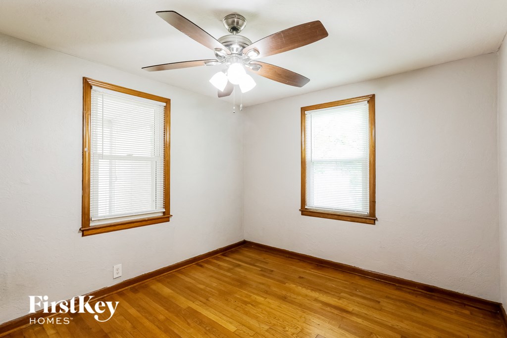 a bedroom with wood floors and a ceiling fan and two windows