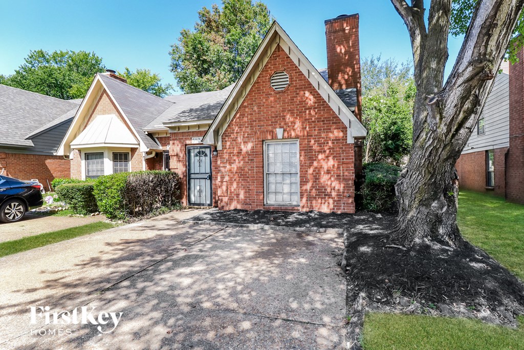 a brick house with a tree and a driveway in front of it
