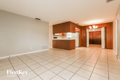 a kitchen and living room with a white tiled floor and wooden cabinets