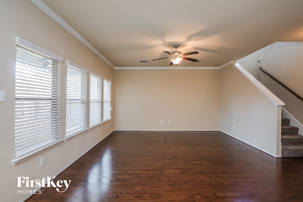 an empty living room with a ceiling fan and large windows
