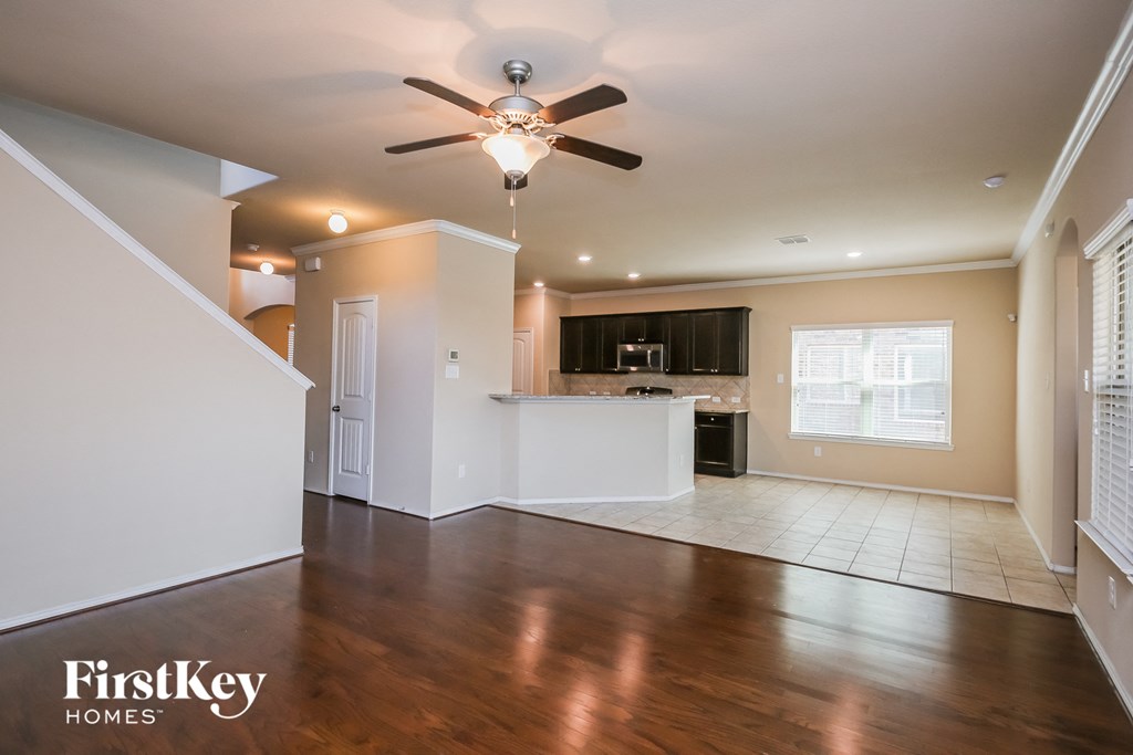 an empty living room with a ceiling fan and a kitchen
