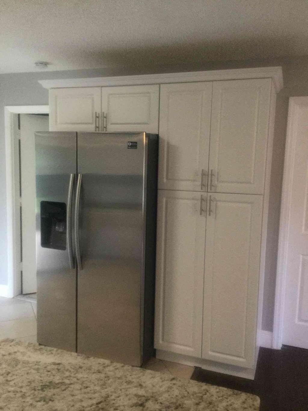 A silver refrigerator with a black door sits next to a white cabinet.