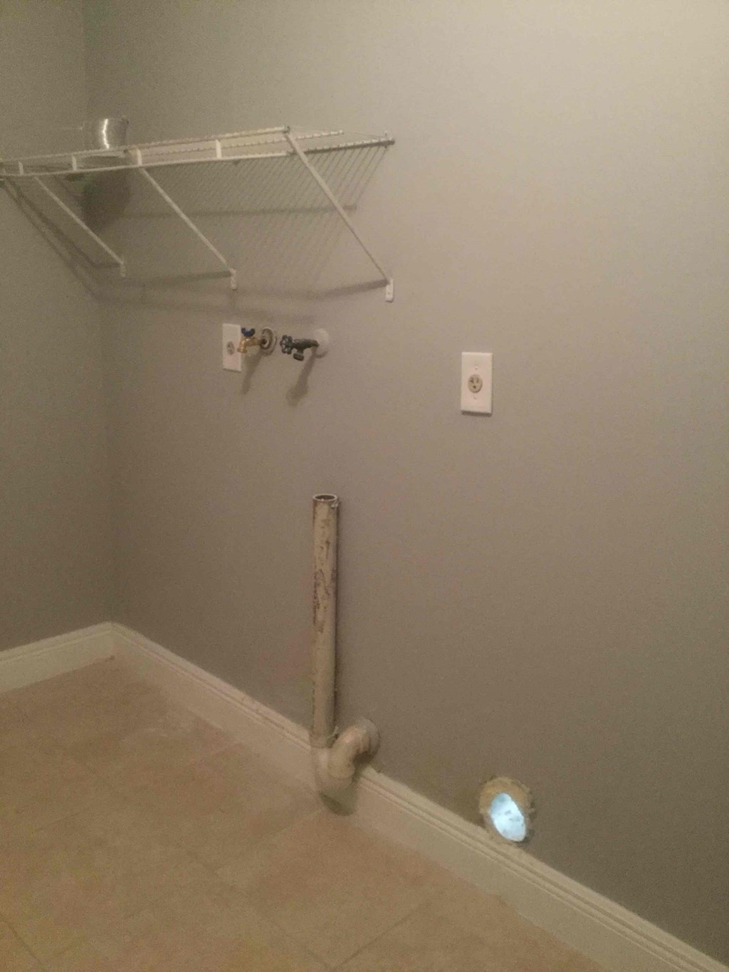 A white shelf is mounted on the wall above a white pipe.