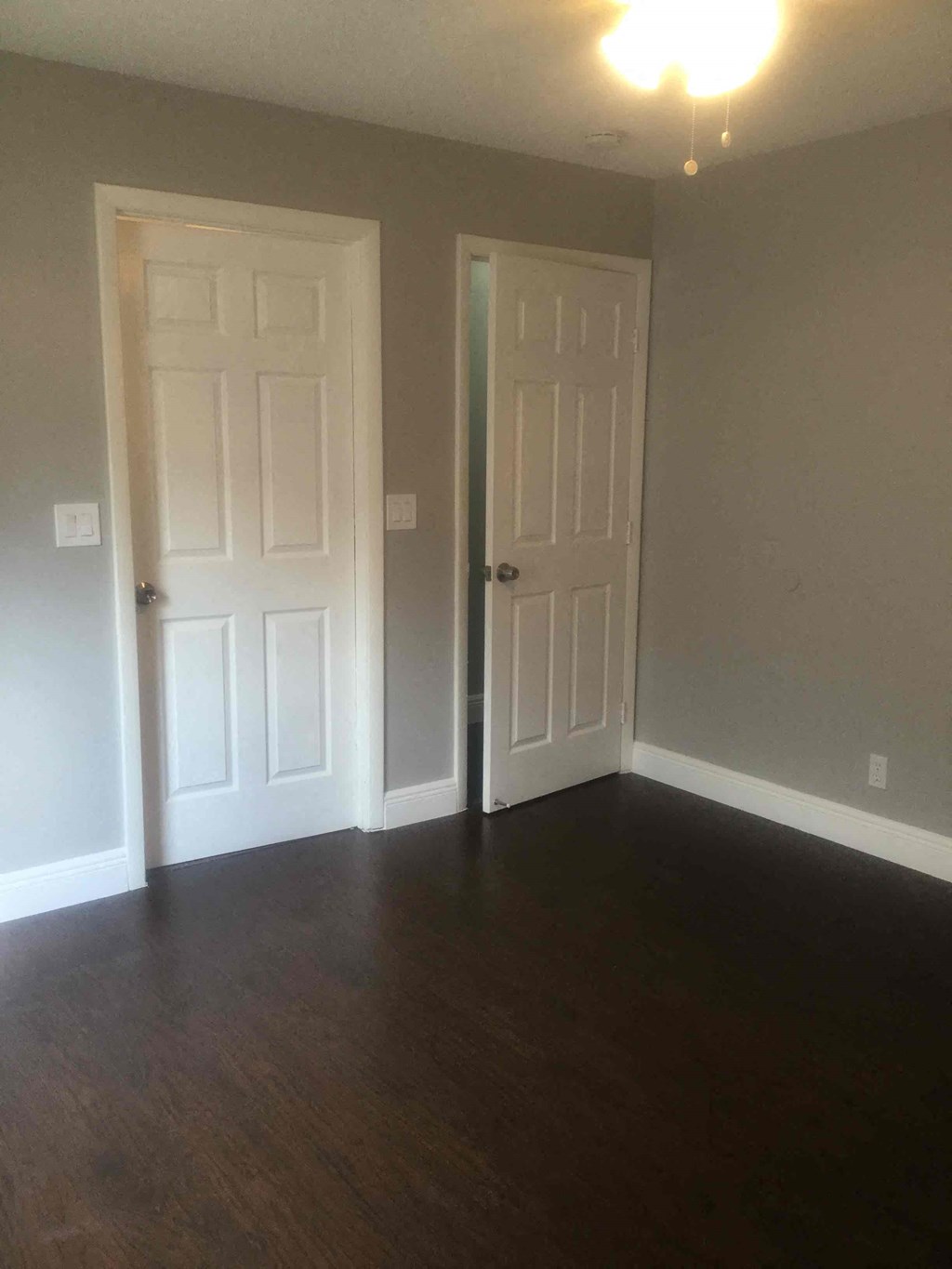 Two white doors in a room with wood floors.