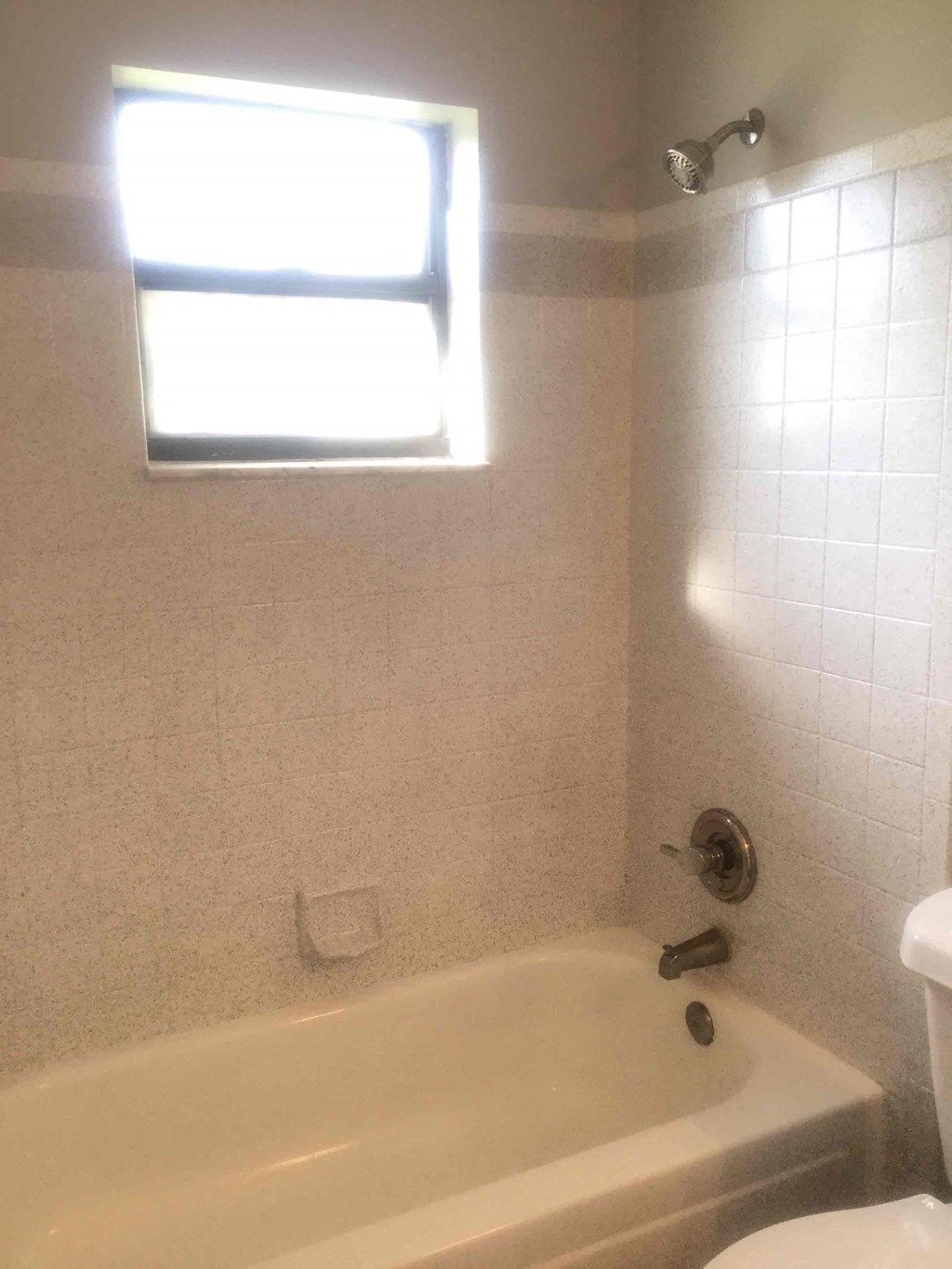A white bathtub sits in a bathroom with a window above it.
