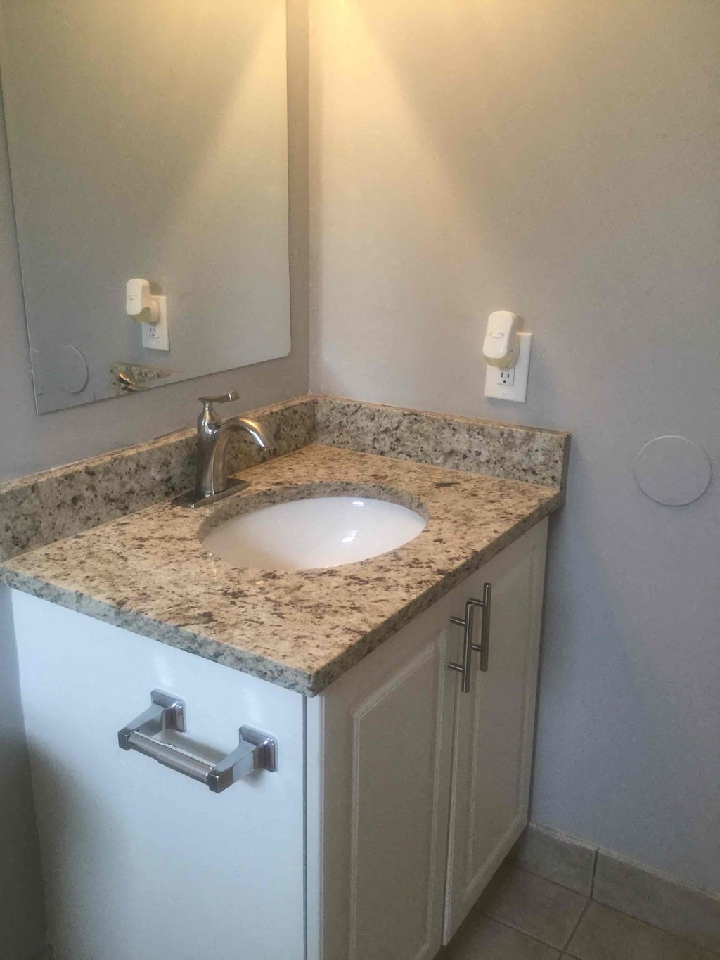 A bathroom sink with a granite countertop and a white cabinet.