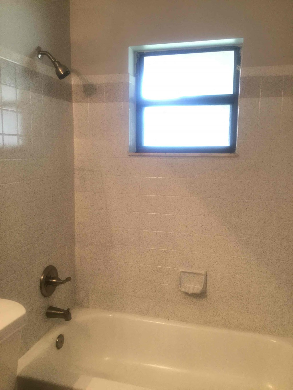 A white bathtub in a bathroom with a window above it.