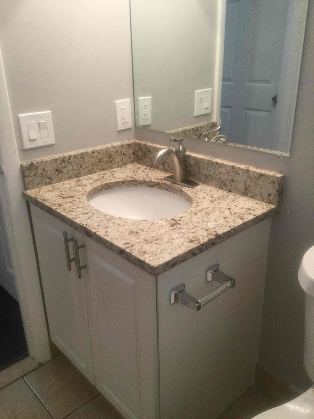 A bathroom sink with a granite countertop and a mirror above it.