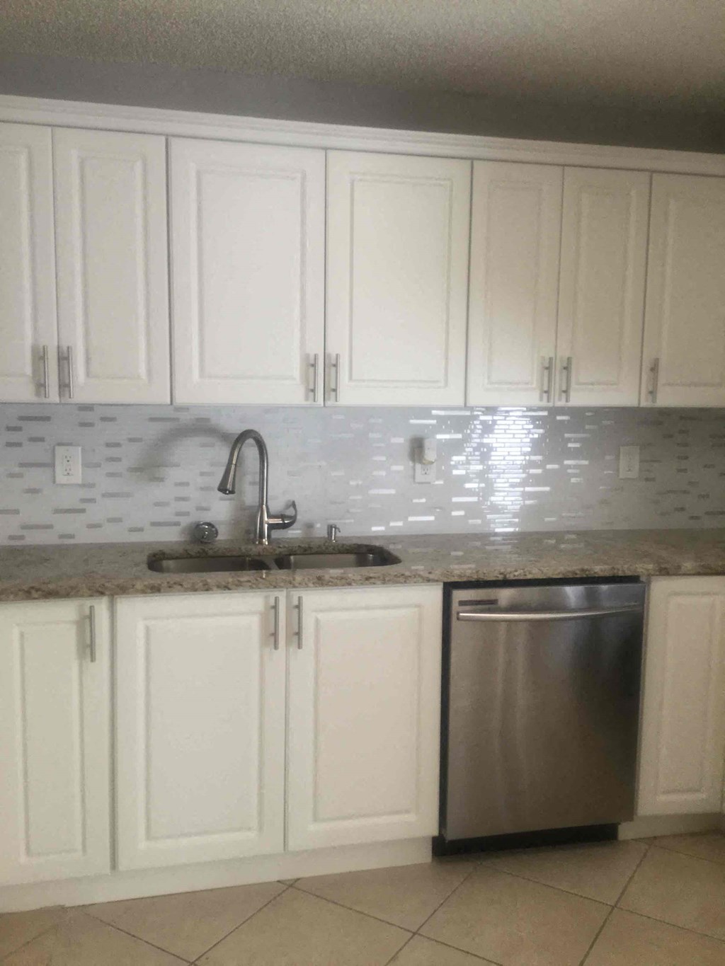 A kitchen with white cabinets and a stainless steel dishwasher.