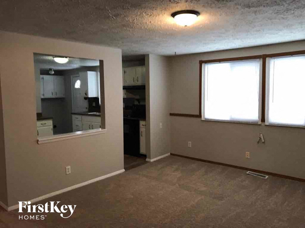an empty living room with a kitchen in the background