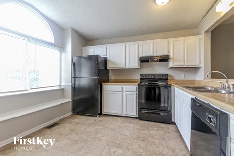 A kitchen with a black fridge, black oven, and white cabinets.