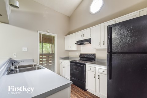 A black refrigerator in a kitchen with white cabinets.
